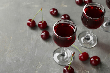 Delicious cherry liqueur in glasses and fresh berries on grey background, space for text