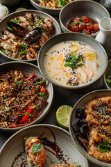 Variety of asian food dishes with seafood, noodles, meat and sesame seeds being served on gray table