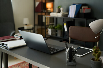 Modern home office setting with laptop on desk surrounded by books, notebooks, and shelves providing an organized and efficient workspace