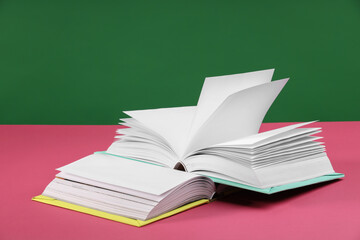 Colorful books on pink table against green background