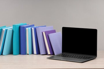 Colorful books and laptop on white wooden table against light grey background