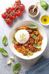 Delicious fresh burrata salad in bowl and ingredients on light gray textured table, flat lay