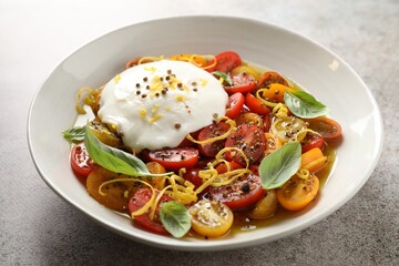 Delicious fresh burrata salad in bowl on gray textured table, closeup