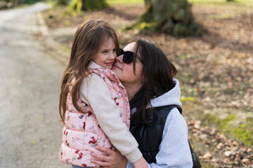 A dark-haired middle-aged girl in sunglasses in an autumn park kisses her little daughter. Happy family life concept