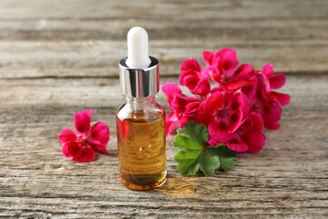 Bottle of geranium essential oil and beautiful flowers on wooden table