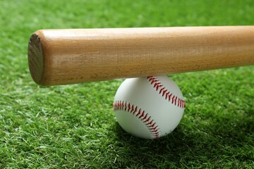 Baseball ball and bat on green grass outdoors, closeup
