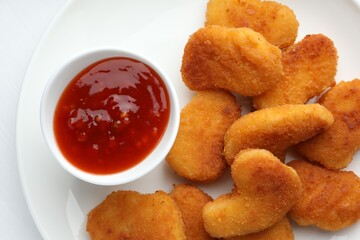 Tasty chicken nuggets with chili sauce on white table, flat lay