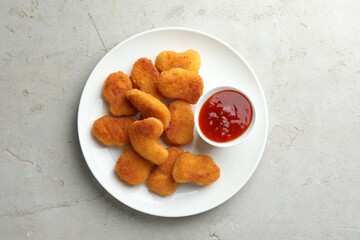 Tasty chicken nuggets with chili sauce on grey textured table, top view