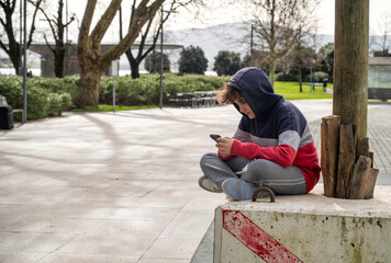 Teenager sitting outdoors, focused on his smartphone