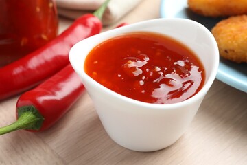Spicy chili sauce in bowl on wooden table, closeup