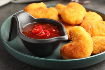 Plate with hot chili sauce and nuggets on grey table, closeup