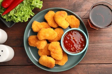 Hot chili sauce and nuggets served on wooden table, flat lay