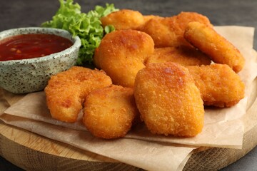 Board with hot chili sauce, lettuce and nuggets on table, closeup