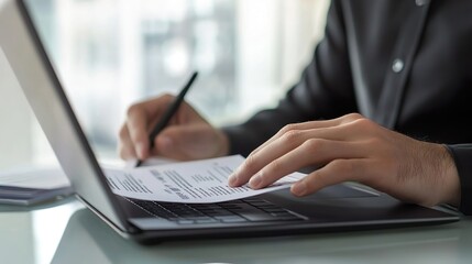 A man is writing on a laptop with a pen