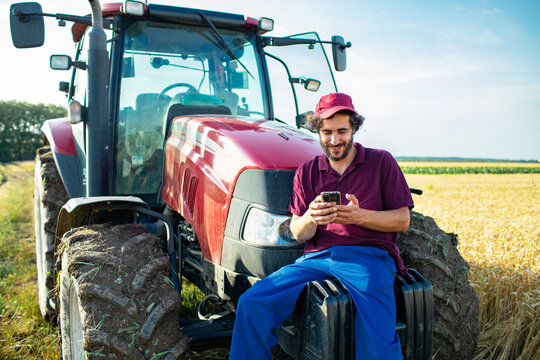 Middle aged male farmer using smartphone on tractor