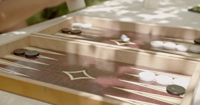 Close-up of a wooden backgammon board with game pieces and dice in an outdoor setting under sunlight. Perfect for themes of leisure, strategy, and traditional games.