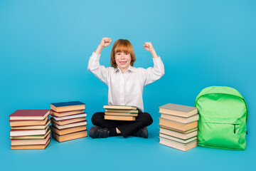 Full size photo of small schoolkid boy pile stack book raise fists wear uniform isolated on blue color background