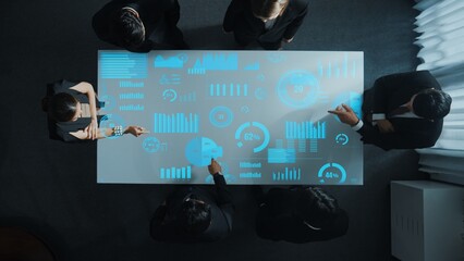 Top down aerial of collaborate professional diverse business people discuss marketing strategy with hologram of marketing data analysis graph, diagram or financial profit investment plan. Directorate.