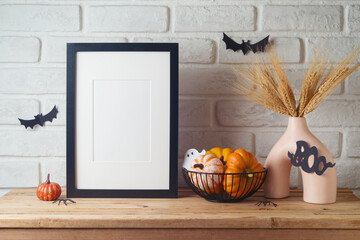 Poster frame mock up for Halloween holiday. Wheat in modern vase and pumpkin decoration on wooden...