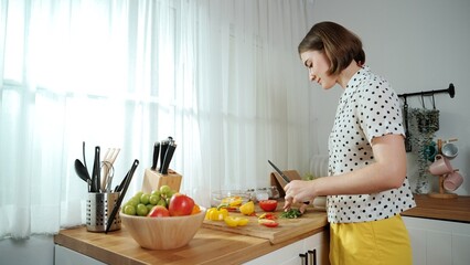 Energetic mother making salad for breakfast at modern kitchen while chopping vegetable surrounded with kitchenware. Smart female house keeper cooking and preparing food. Healthy lifestyle. Pedagogy.