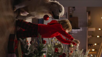 Boy and his faithful big dog joyfully prepare for Christmas by decorating tree with red balls, eagerly awaiting arrival of New Year. Festive spirit, joy happiness, Santa Claus. Cinematic vertical AD - Powered by Adobe