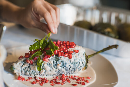 Preparation of the famous chiles en Nogada, traditional Mexican food in the month of September, stuffed chile being covered by the nogada which is a cream with walnut and hand adding parsley.