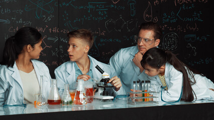 Multicultural student looking under microscope while cute girl inspect sample. Teacher looking...