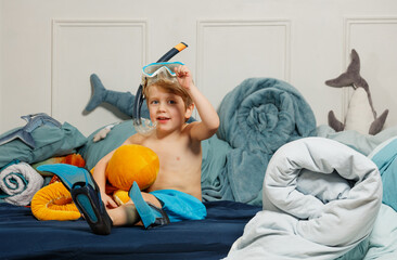 Boy wearing snorkel sitting on bed with stuffed sea creatures