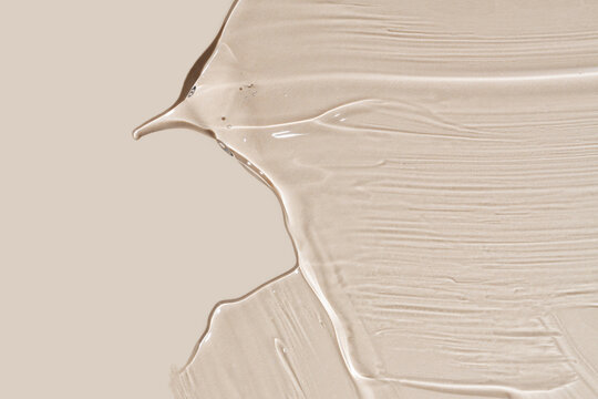 Close-up shot of beige liquid cosmetic gel or serum makeup swatches with a glossy, shiny texture on a smooth beige background.