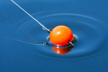 Orange fishing bobber floating on blue water with line attached. Generated by AI.