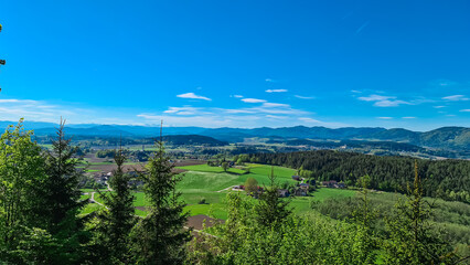 Alpine landscape with church in small village Stein im Jauntal nestled amidst rolling hills and lush greenery. Majestic mountain range with snow-capped peaks in Carinthia. Breathtaking backdrop