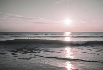 Obraz premium A serene ocean landscape with calm, rippling waves reflecting the warm, pastel-colored sky and bright sun in the distance