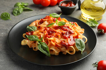 Delicious pasta with tomato sauce and basil on grey textured table, closeup