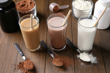 Delicious protein shakes in glasses, powder and spoons on wooden table