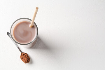 Delicious protein shake in glass and spoon with powder on white background, top view. Space for text