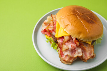 Delicious burger with bacon, patty and cheese on green background, space for text