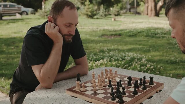 Two men playing a strategic game of chess on a park bench. The intense concentration is evident on their faces as they contemplate their next moves.