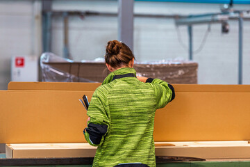 Worker in a green jacket inspecting packaging materials in an industrial warehouse, ensuring...