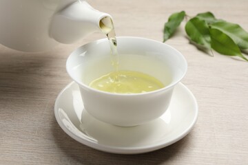 Pouring refreshing green tea into cup at wooden table, closeup
