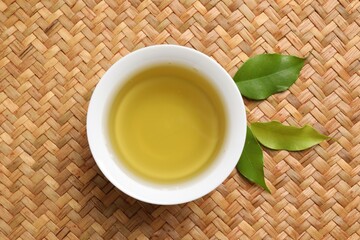 Refreshing green tea in cup and leaves on table, flat lay