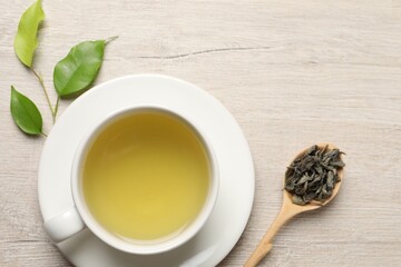 Refreshing green tea in cup, spoon and leaves on wooden table, flat lay