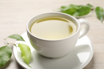 Refreshing green tea in cup and leaves on wooden table, closeup