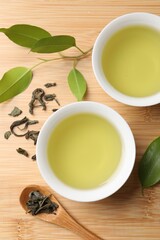 Refreshing green tea in cups, spoon and leaves on wooden table, flat lay