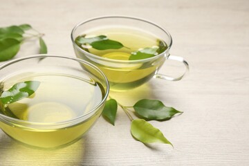 Refreshing green tea in cups and leaves on wooden table, closeup