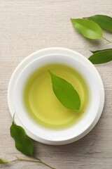 Refreshing green tea in cup and leaves on wooden table, flat lay