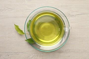 Refreshing green tea in cup and leaves on wooden table, top view