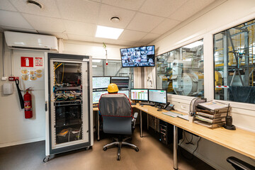 Control room in an industrial facility with multiple monitors displaying live feed and system controls for machinery operation