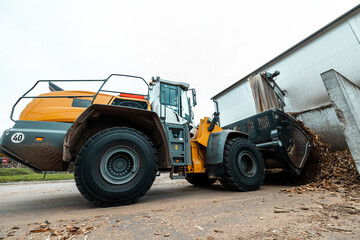 Fototapeta premium Yellow industrial wheel loader in action, transporting wood chips outside a facility