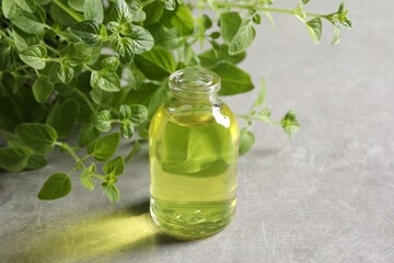 Essential oil in bottle and oregano twigs on light grey textured table, closeup. Space for text