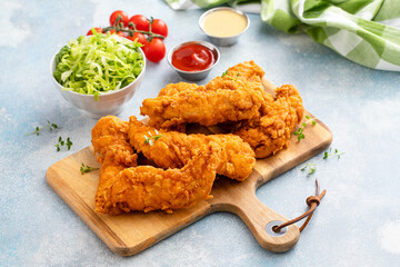 Fried chicken tenders on a serving board with sauces and salad